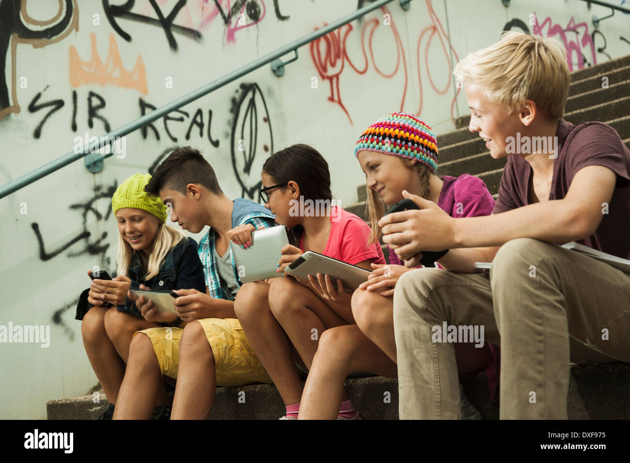 Gruppe von Kindern auf Treppen im Freien, sitzend mit Tablet-PCs und Smartphones, Deutschland Stockfoto