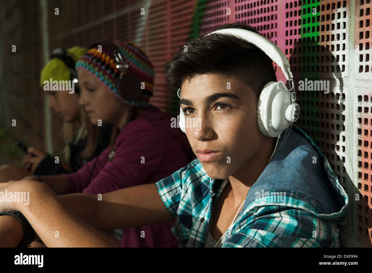 Close-up Portrait von Junge sitzt neben Wand, tragen von Kopfhörern und Musik hören, andere Kinder im Hintergrund, Deutschland Stockfoto