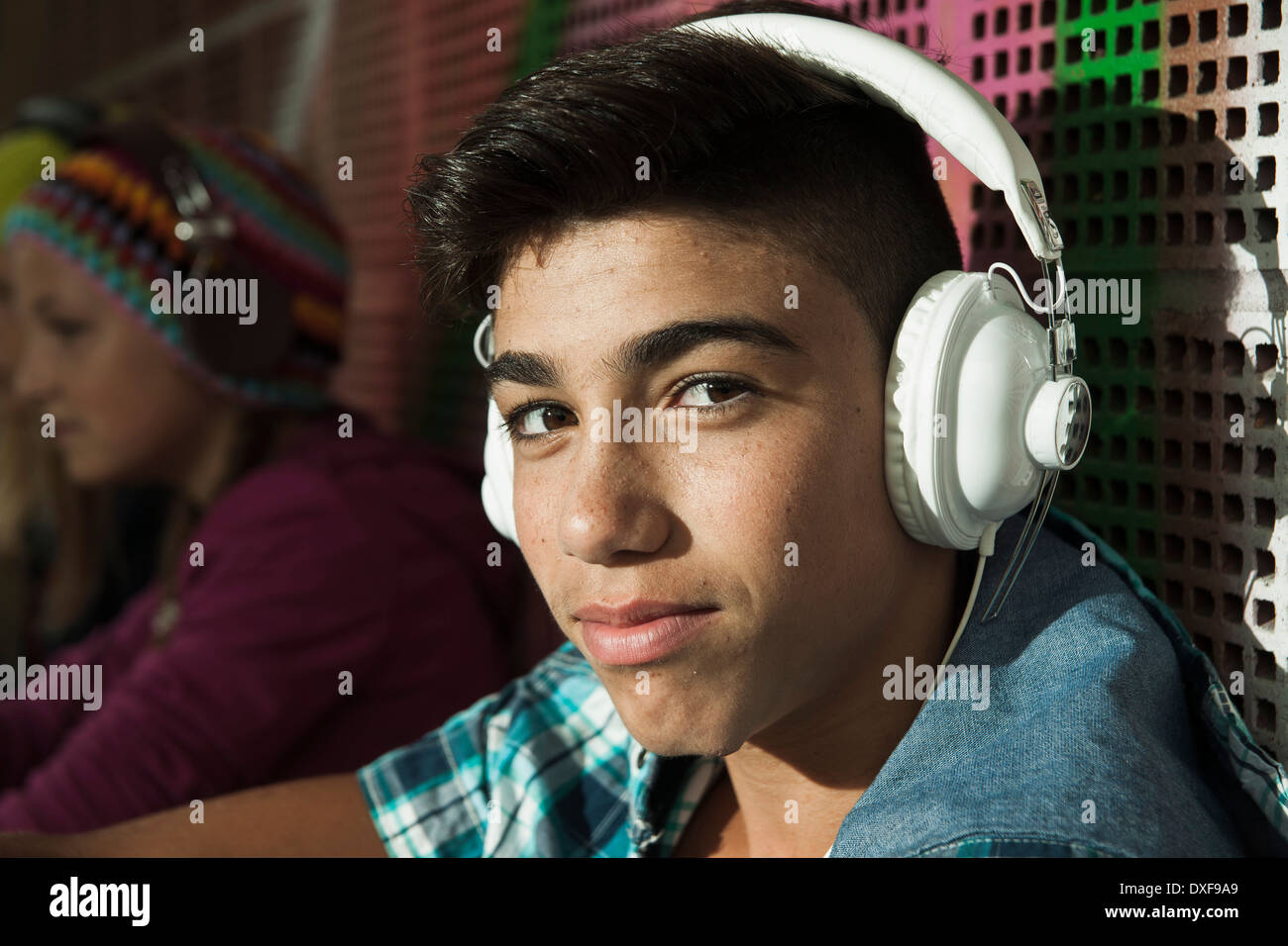 Close-up Portrait von Junge sitzt neben Wand im Freien, tragen von Kopfhörern und Blick in die Kamera, Deutschland Stockfoto