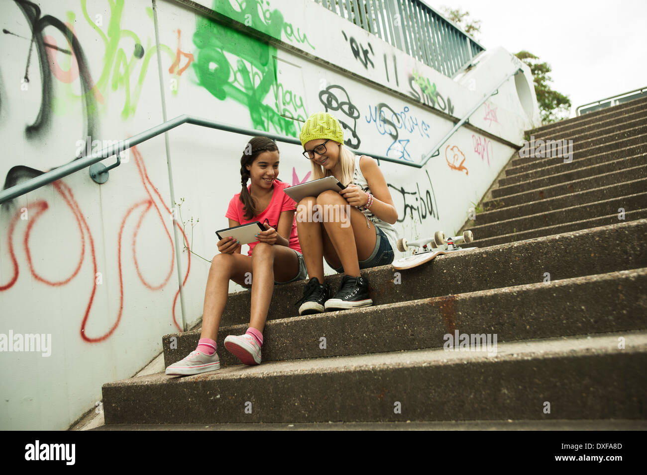 Mädchen sitzen auf Stufen mit Tablet-PCs und Skateboard, Mannheim, Baden-Württemberg, Deutschland Stockfoto