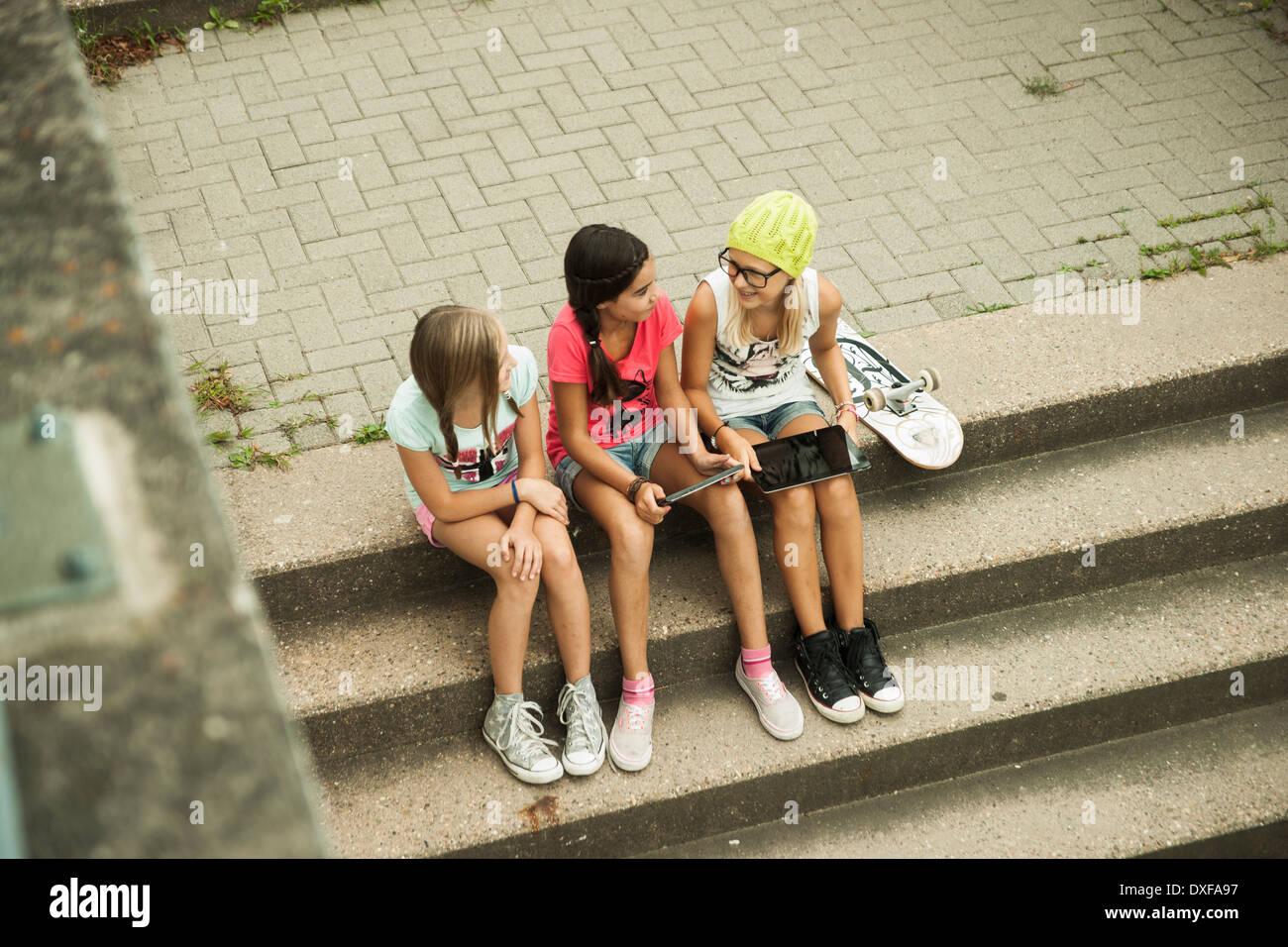 Mädchen sitzen auf Stufen mit Tablet-PCs und Skateboard, Mannheim, Baden-Württemberg, Deutschland Stockfoto