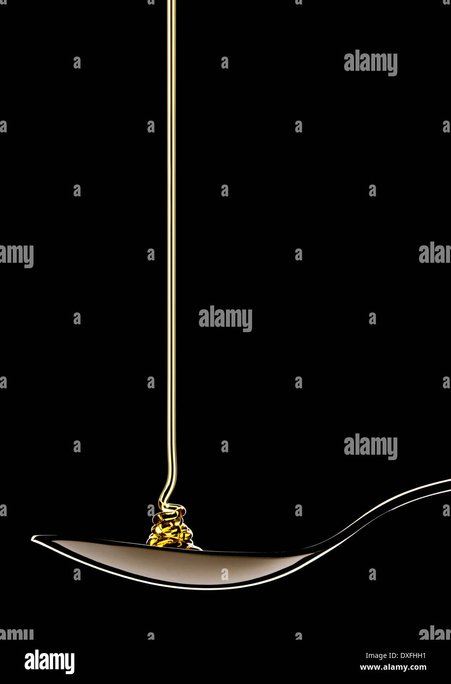 Sirup - Sirup - Gießen auf Metalllöffel auf schwarzem Hintergrund. Stockfoto