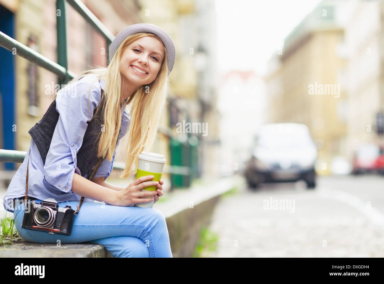 Glückliche junge Hipster sitzen in der Stadt mit Tasse Heißgetränk Stockfoto