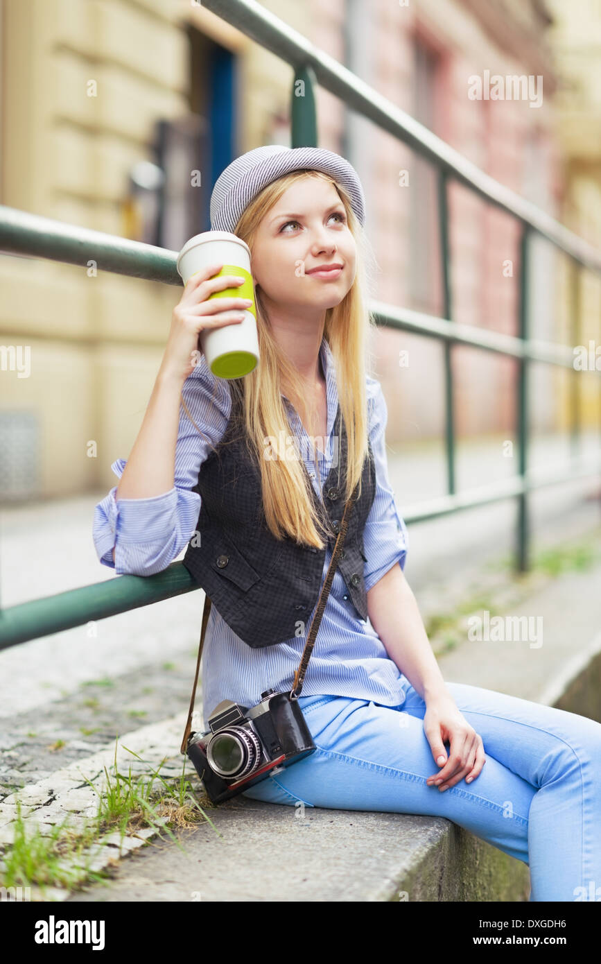 Junge Hipster sitzen in der Stadt mit Tasse Heißgetränk Stockfoto