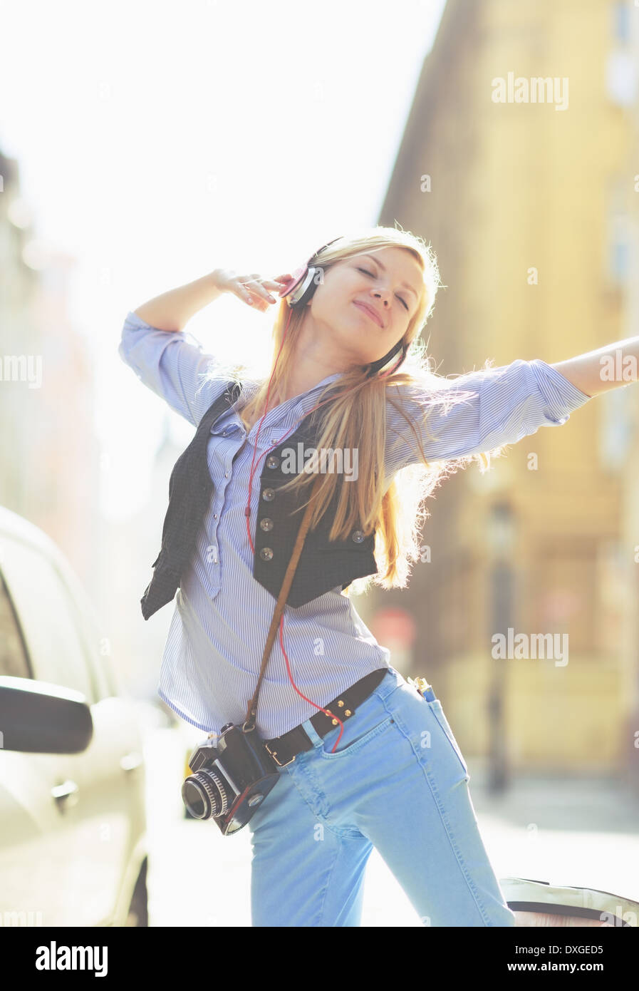 Fröhliche junge Frau hören von Musik im Kopfhörer in der Stadt Stockfoto