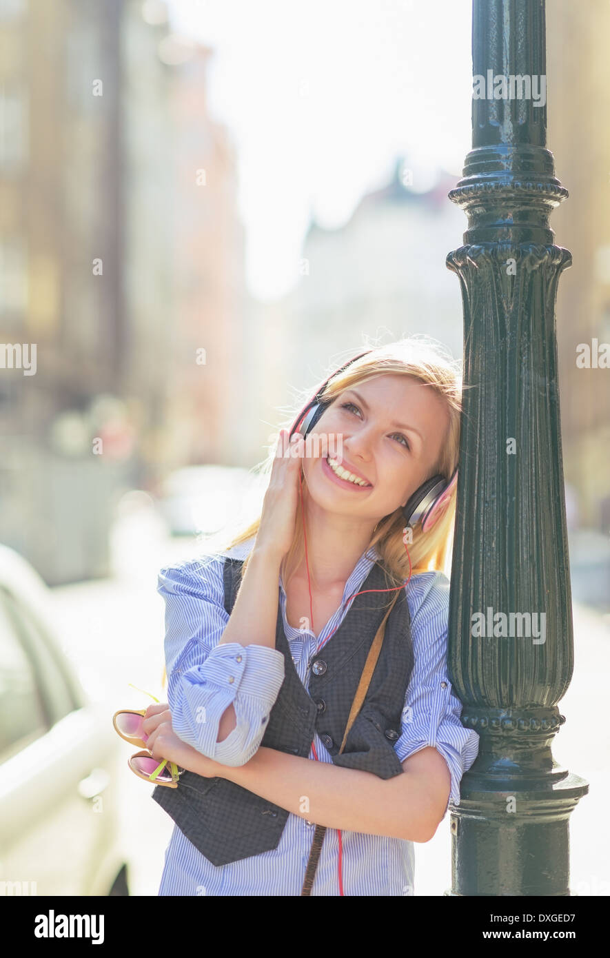 Glückliche junge Frau hören von Musik im Kopfhörer in der Stadt Stockfoto