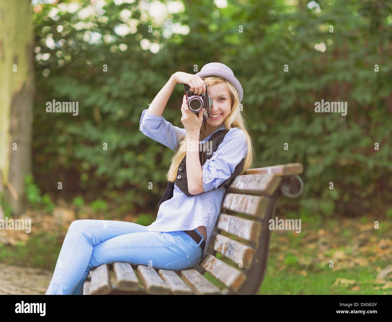 Junge Hipster nehmen Foto mit Retro-Foto-Kamera sitzt auf der Bank im park Stockfoto