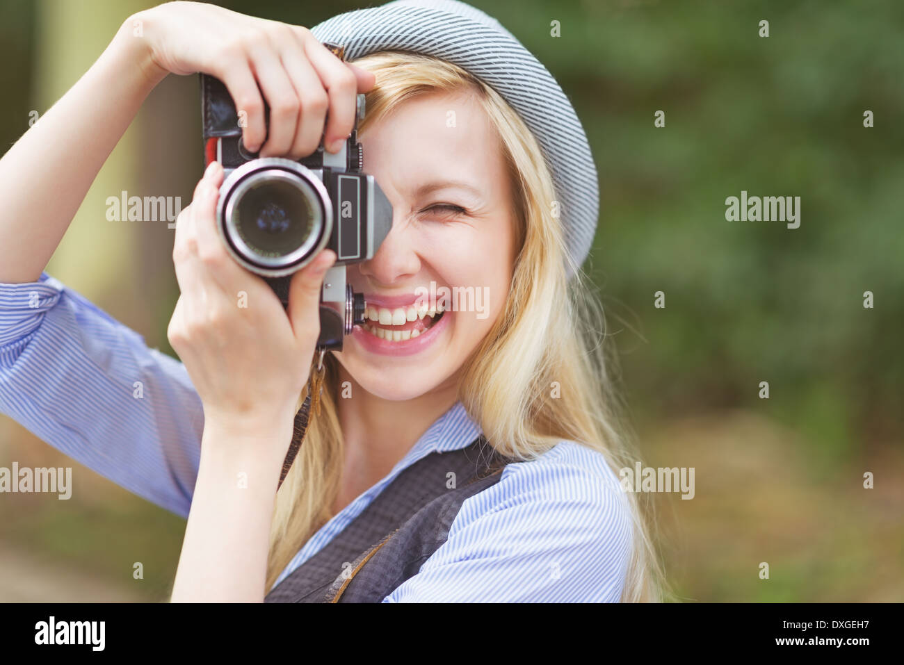 Glückliche junge Hipster nehmen Foto mit Retro-Foto-Kamera sitzt auf der Bank im park Stockfoto