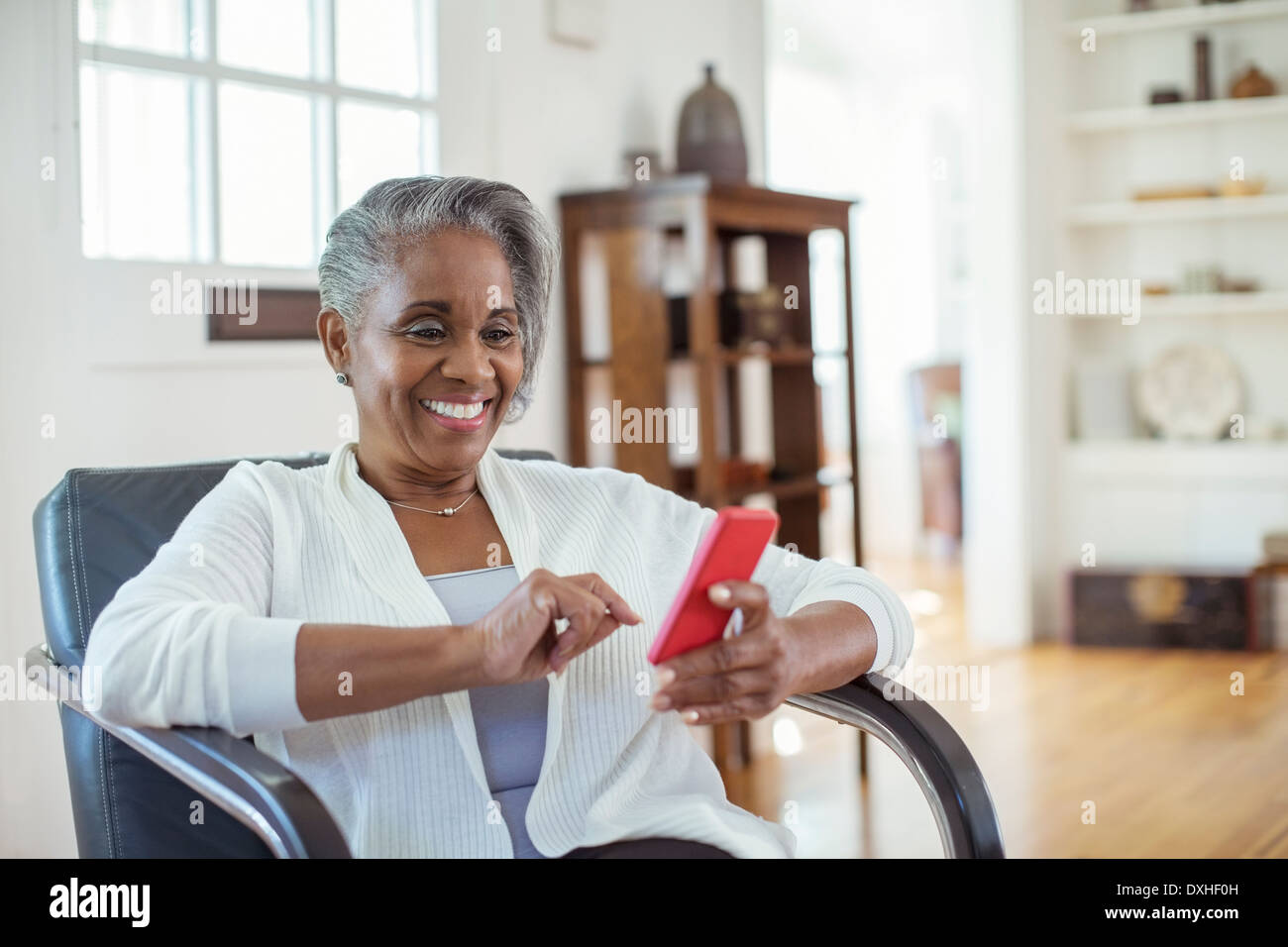 Beautiful senior Woman Text messaging mit Handy im Wohnzimmer Stockfoto