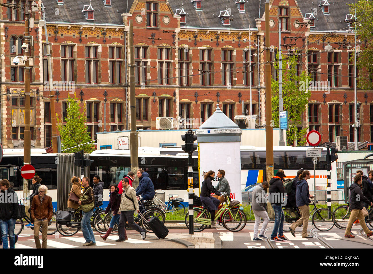 Fußgänger zu Fuß über einen Fußgängerüberweg am Damrak in Amsterdam. Der Bahnhof Centraal ist im Hintergrund. Stockfoto