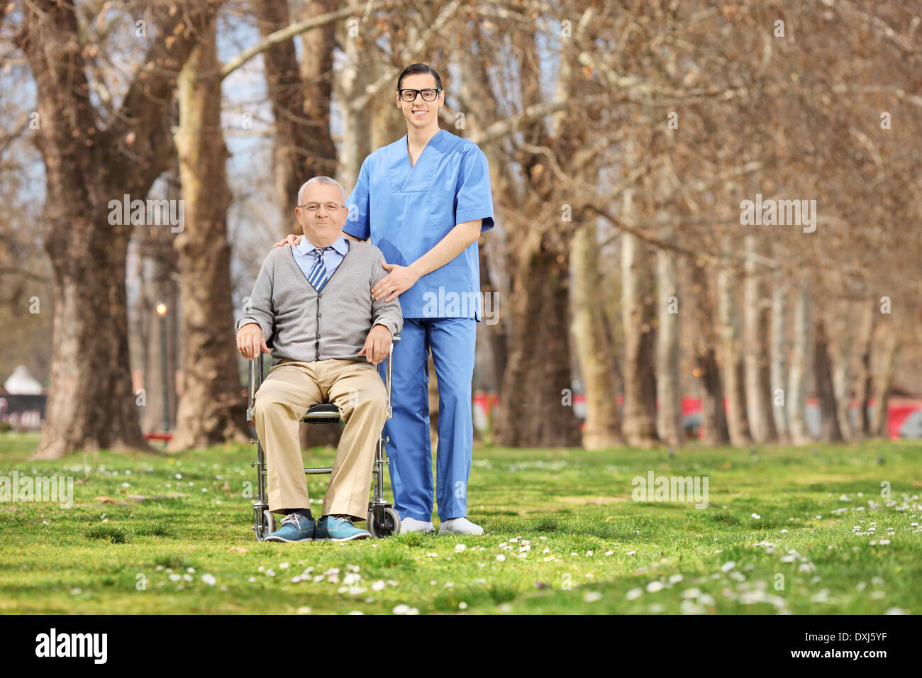 Mann im Rollstuhl und Krankenpfleger posiert im Park an einem sonnigen Tag Stockfoto