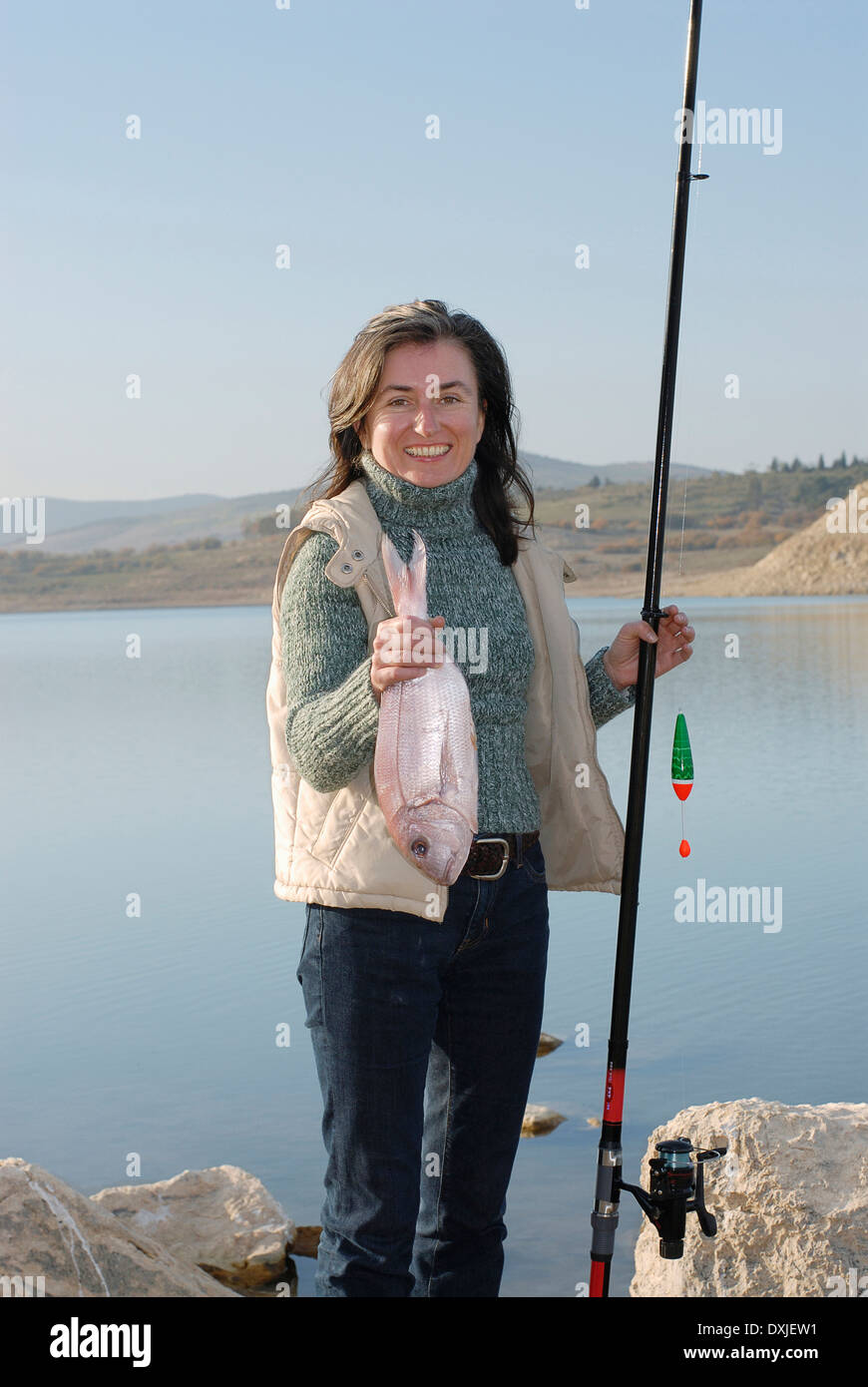 Reife Frau am Seeufer mit Angelrute und Fisch, Lächeln, Porträt Stockfoto