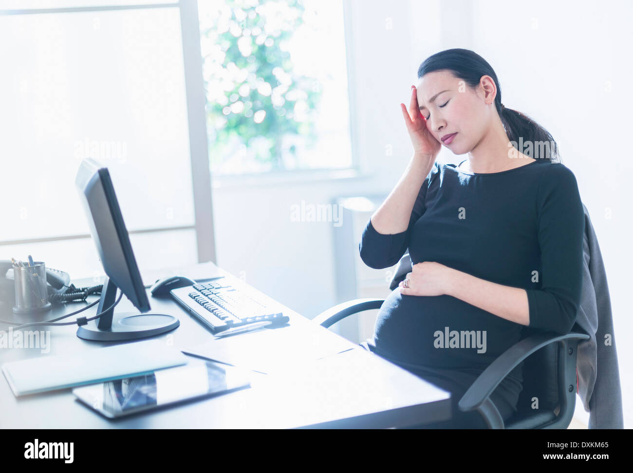 Müde schwanger japanische Geschäftsfrau am Schreibtisch Stockfoto