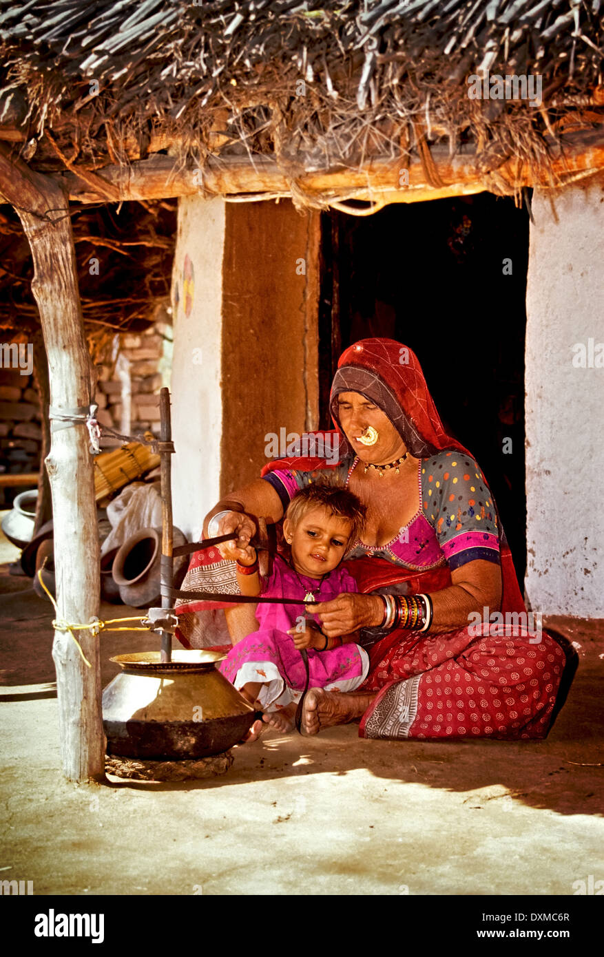 Indische Frau hält ein Kind und Mahlen von Mehl in einem Dorf in der Nähe von Jodhpur, Indien. Digital manipulierte Bild. Stockfoto