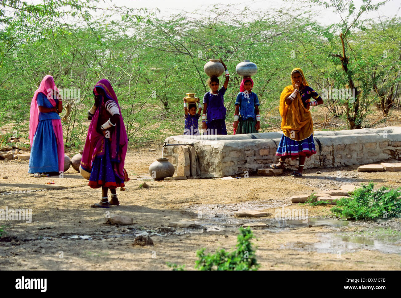 Indische Frauen sammeln Wasser in Flaschen, Gläser auf dem Kopf tragen Stockfoto