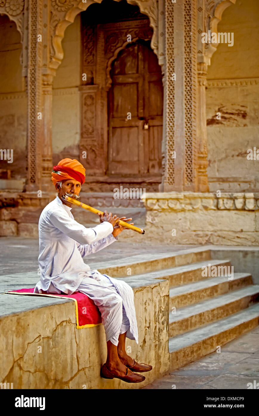 Indischer Musiker sitzt auf einer Mauer Flötenspiel in Mehrangarh Fort in Jodhpur, Indien. Digital manipulierte Bild. Stockfoto