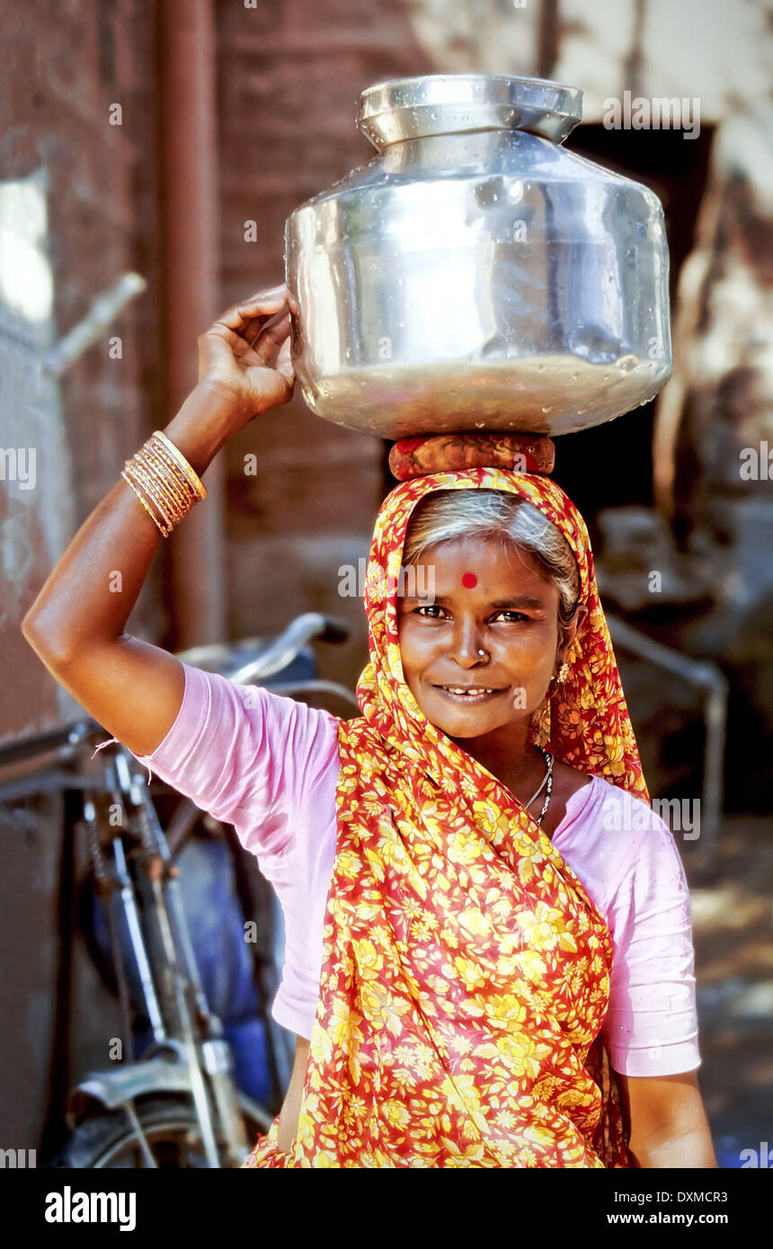 Indische Frau trägt einen bunten Schal mit einem Edelstahl-Wasser-Topf auf dem Kopf. Stockfoto