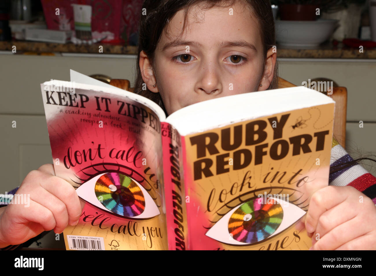 9 Jahre altes Mädchen sitzen am Küchentisch, lesen ein Buch Ruby Redfort Surrey England Stockfoto