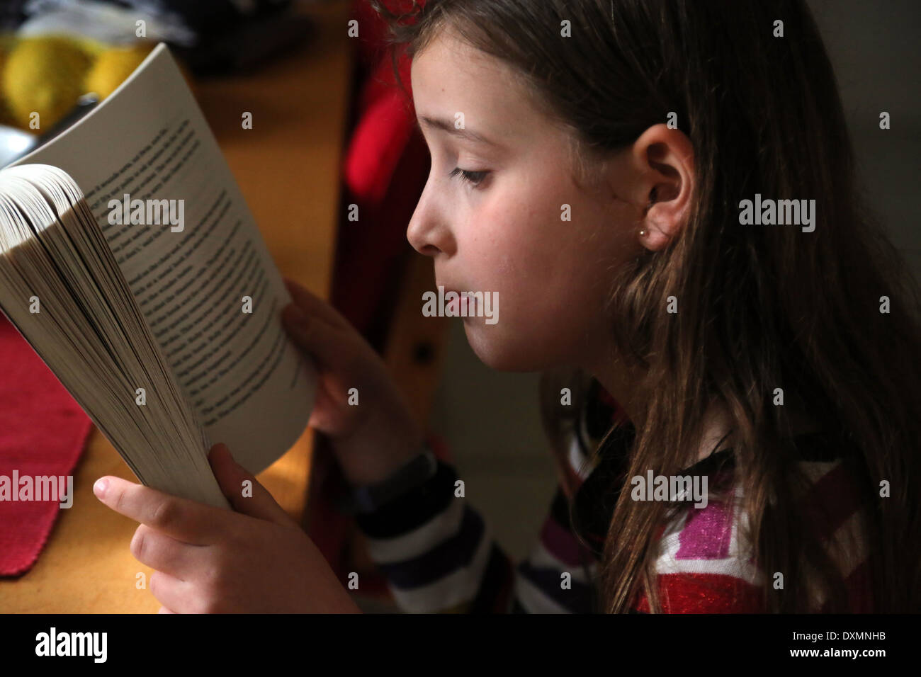 9 Jahre altes Mädchen sitzen am Küchentisch, lesen ein Buch Ruby Redfort Surrey England Stockfoto