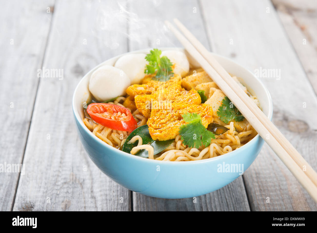 Scharfes Curry instant-Nudelsuppe mit Stäbchen am Esstisch aus Holz. Frisch gekocht, heiß mit gedünstetem Rauch. Stockfoto