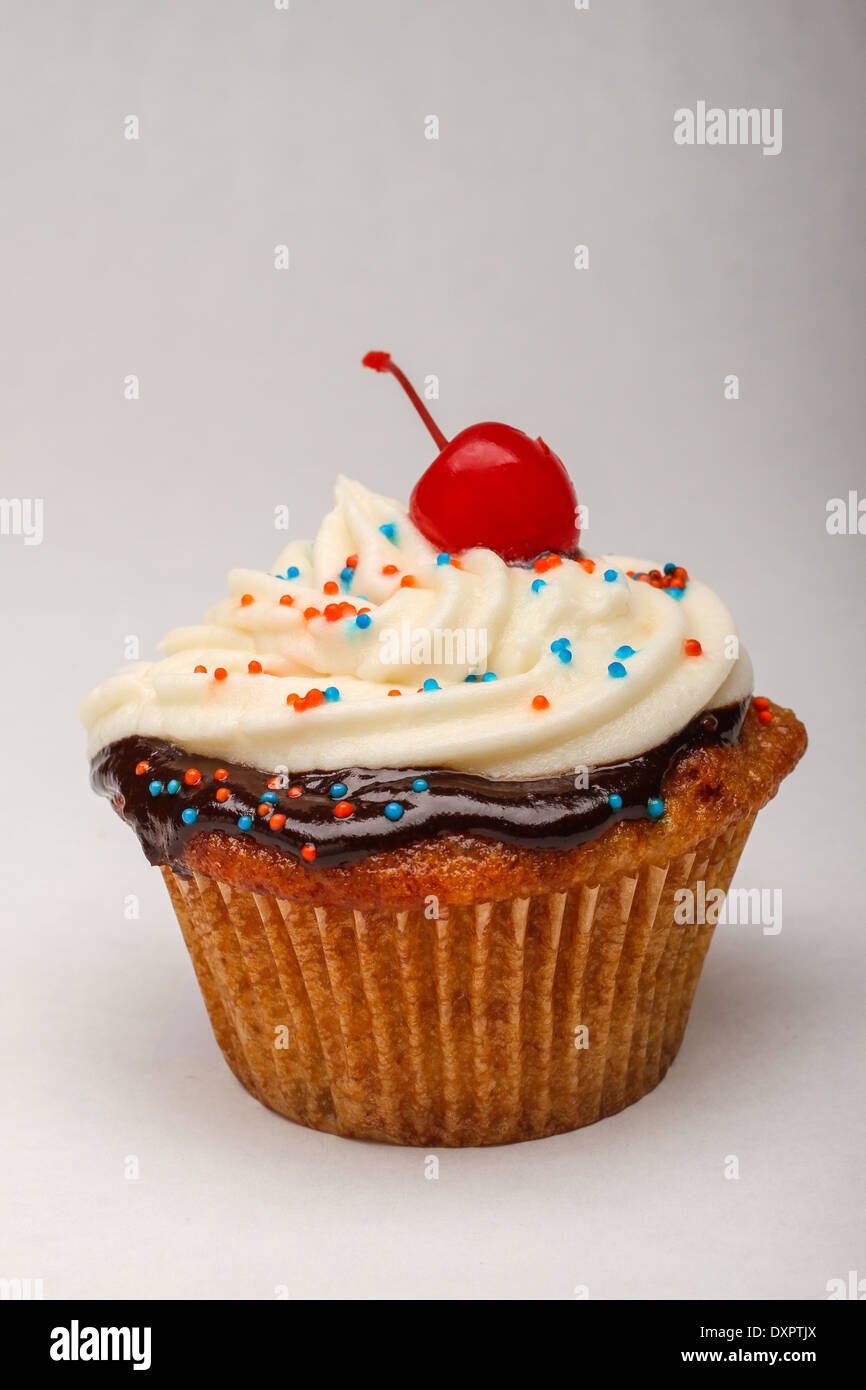 Ein Cupcake mit Schokoladenganache, Buttercremefeisung, bestreuen und einer Kirsche. Stockfoto