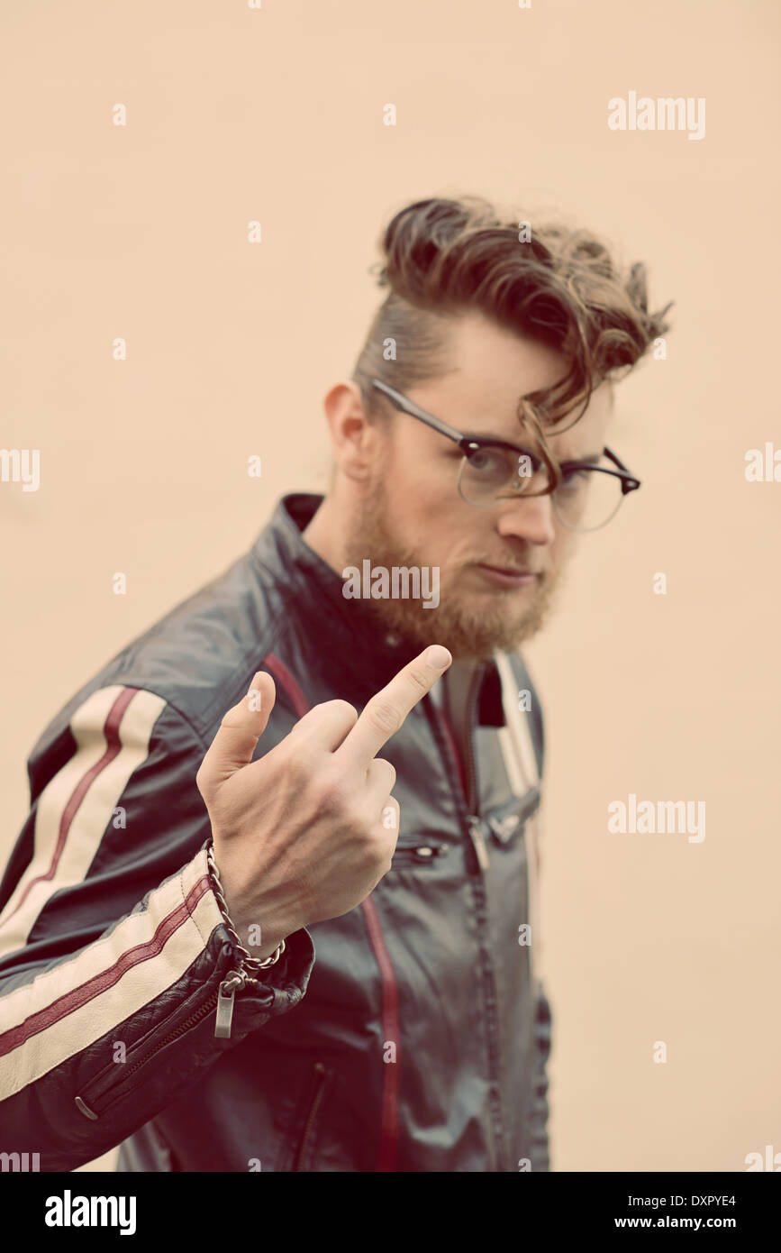 Ein bärtiger Mann in Vintage Pompadour Frisur und Vintage Brillen spiegeln seinen Mittelfinger, eine trendige Vintage Porträt-Konzept Stockfoto