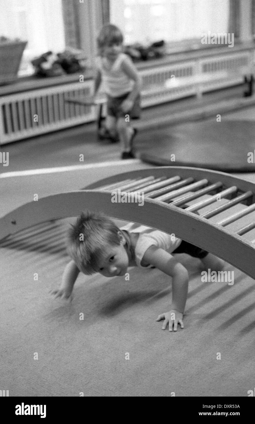 Berlin, DDR, Kind krabbelt in einer Kindertagesstaette unter einem hölzernen Gitter durch Stockfoto