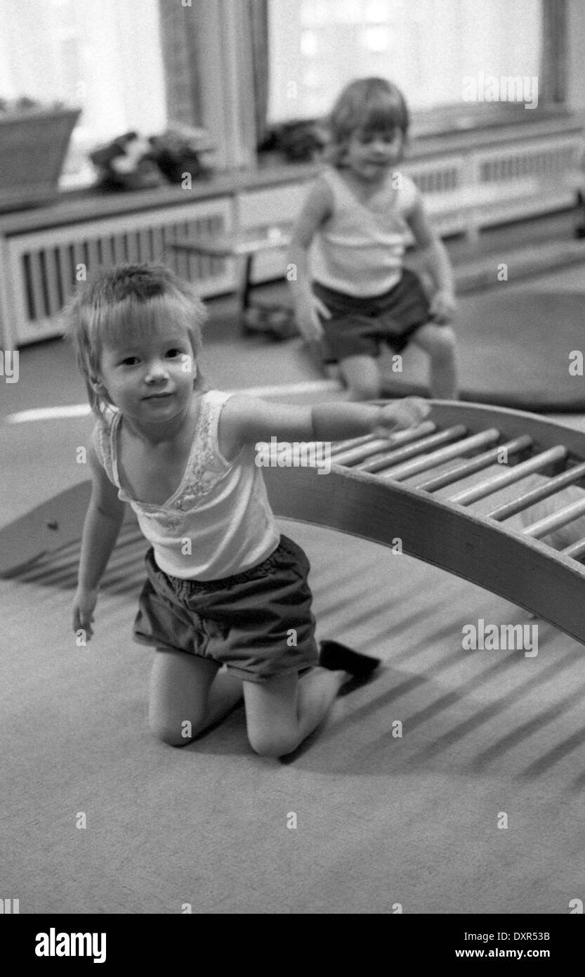 Berlin, DDR, Kind krabbelt in einer Kindertagesstaette unter einem hölzernen Gitter durch Stockfoto