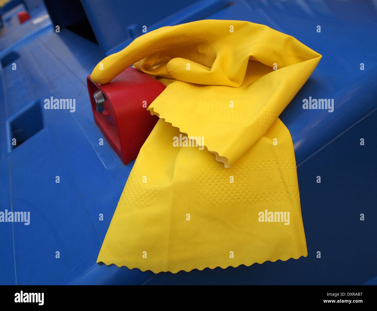 gelben Gummihandschuh auf einem blauen Mülleimer Stockfoto