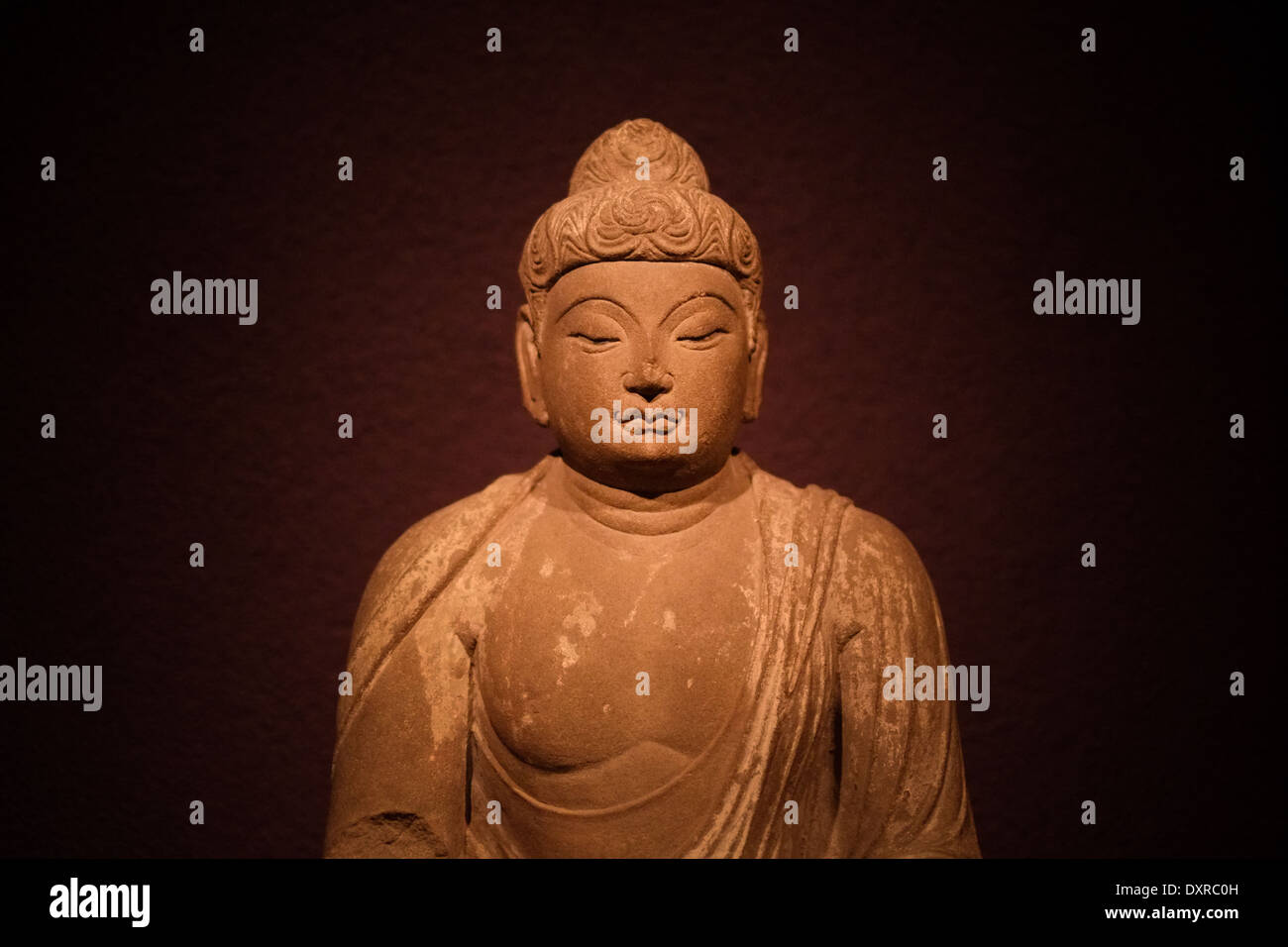 Foto einer alten Buddha-Skulptur von einem Scheinwerfer vor einem dunklen lila Hintergrund beleuchtet. Stockfoto