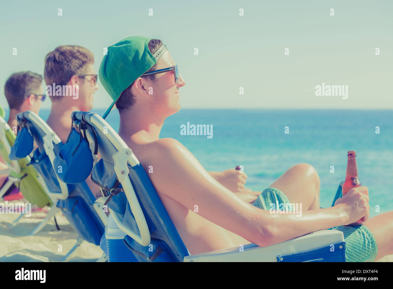 Junge Männer trinken Bier in Liegestühlen am Sonnenstrand Stockfoto