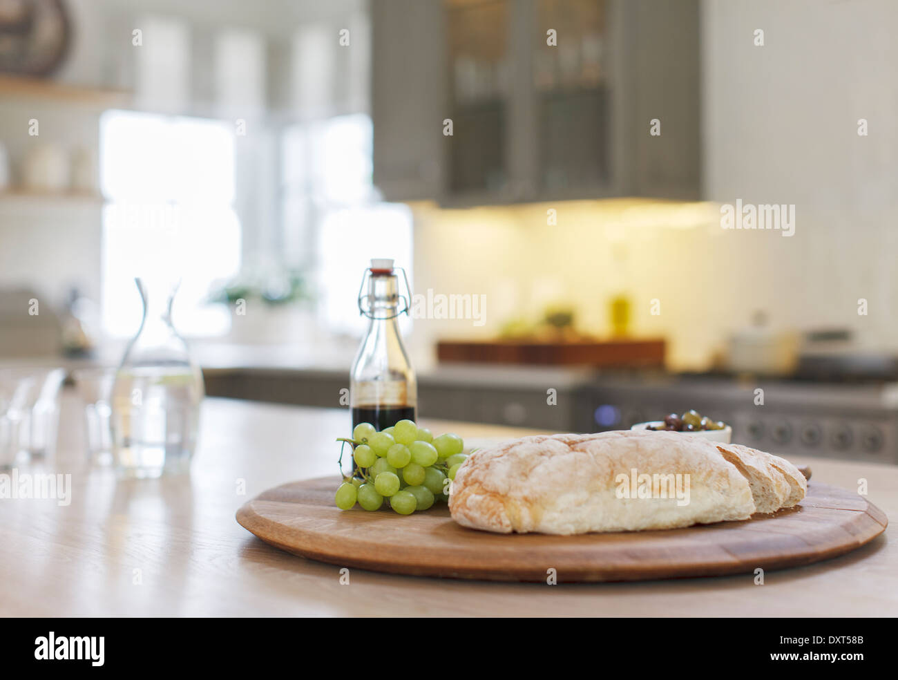 Baguette, Balsamico-Essig und Trauben auf Holzbrett in Küche Stockfoto