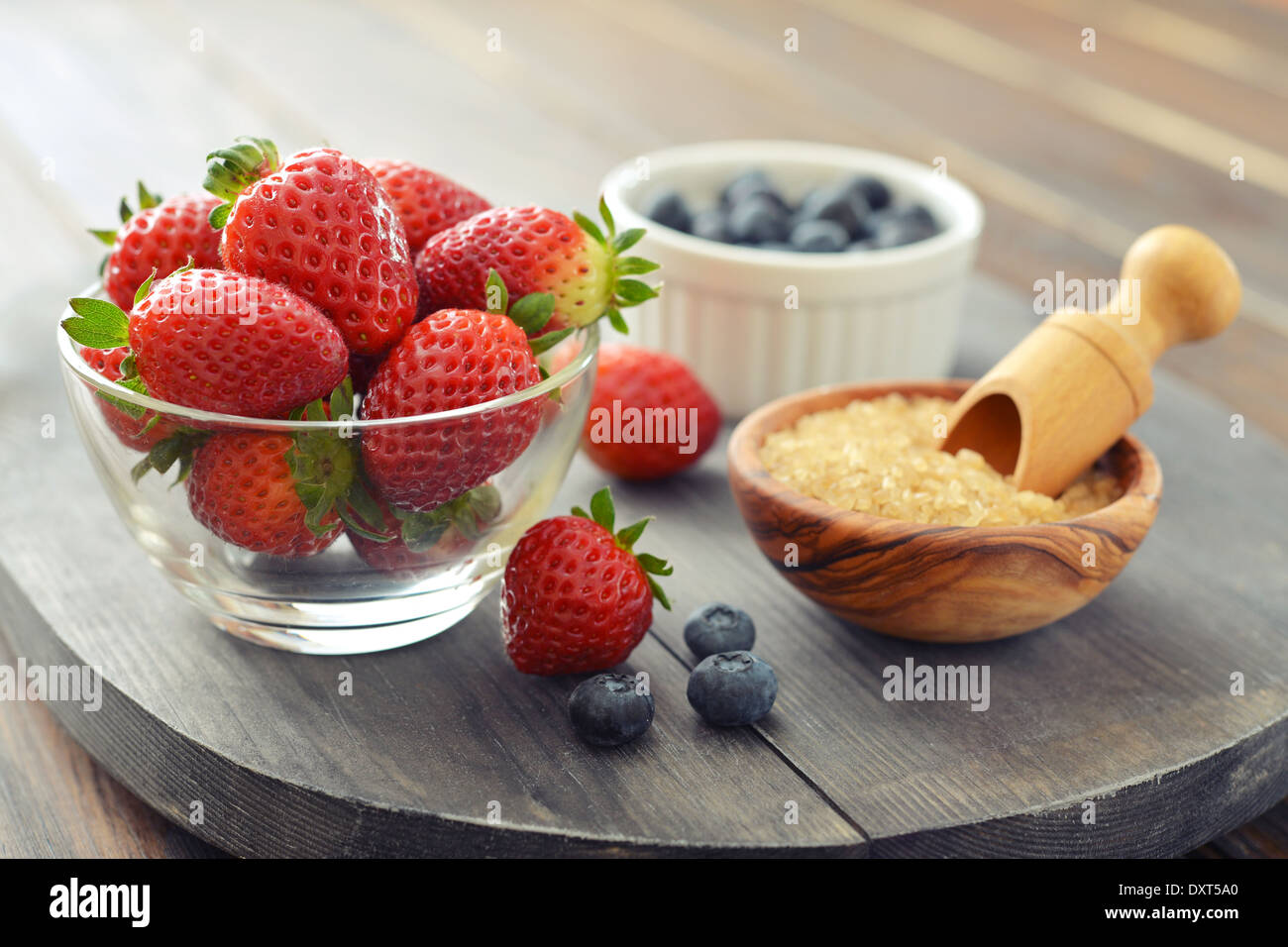 Frische Erdbeeren in Glasschale mit Heidelbeeren und Zucker auf hölzernen Hintergrund Stockfoto