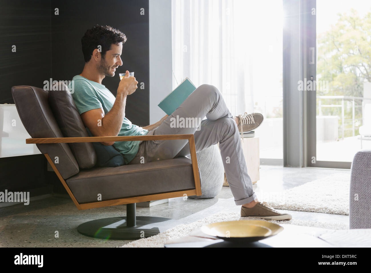 Mann, Tee trinken und Lesebuch im Wohnzimmer Stockfoto