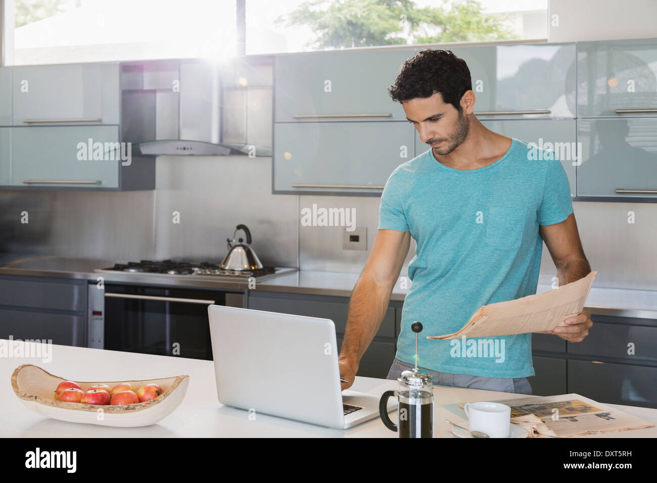 Mann mit Zeitung mit Laptop in der Küche Stockfoto