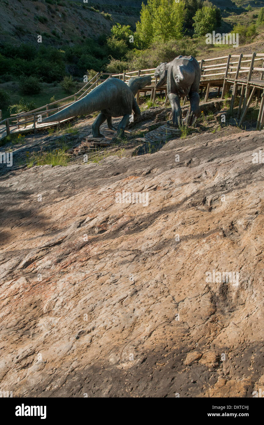 Ornithopod Dinosaurier Fußabdrücke (oder Ichniten) in einem flachen Felsen, früher der Boden einer Binnenlagune an der Virgen del Campo Fossilienstelle, La Rioja, Spanien. Ein paar kämpfende Dinosaurier-Modelle wurden platziert, um die Geschichte, die durch die Fußabdrücke erzählt wird, nachzubilden. Stockfoto