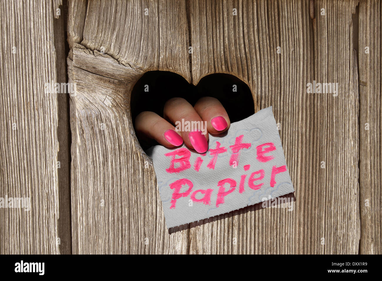 Hand, die eine Notiz, "Bitte Papier", Deutsch für "Bitte Paper", durch das herzförmige Loch eines WC-Hauses Stockfoto