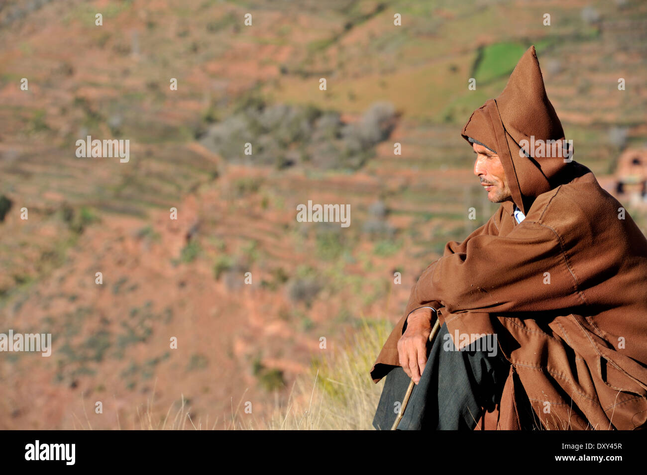 Mann im Umhang mit Kapuze sitzen Blick auf weit entfernten Raum Stockfoto