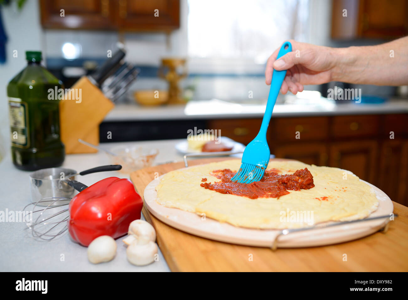 Mann Bürsten Tomatensoße über den Teig auf eine heiße Steinbackplatte für die Herstellung einer hausgemachten pizza Stockfoto