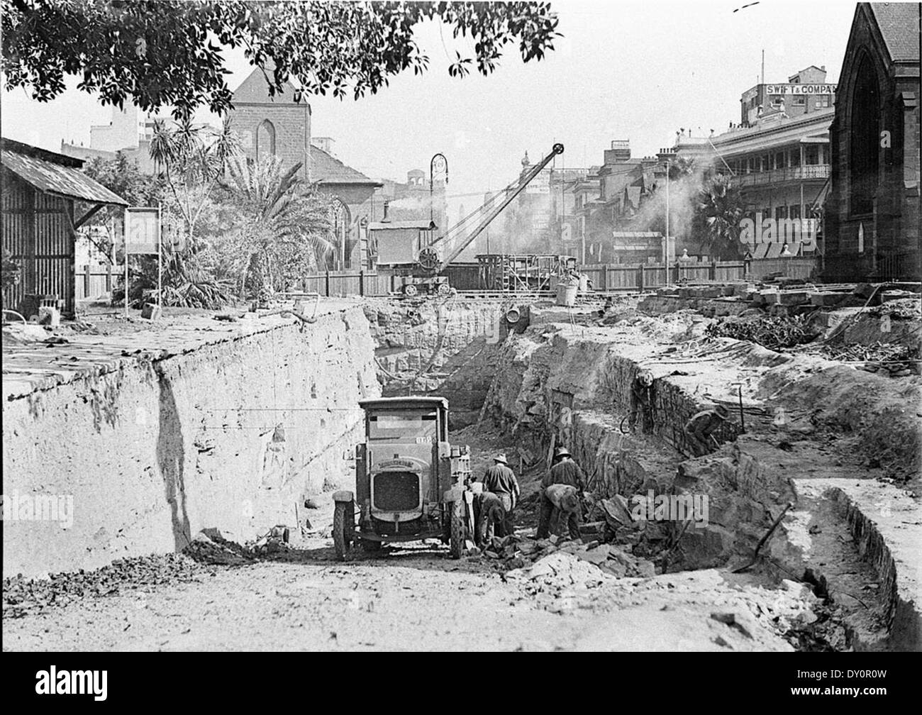 Dieses Foto zeigt die frühen Ausgrabungen auf der York Street für den südlichen Zugang zur Sydney Harbour Bridge, mit bemerkenswerten Wahrzeichen wie der Scots Church und der St. Philips Church im Hintergrund. Stockfoto