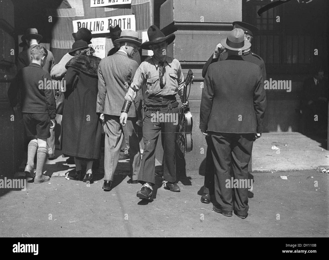 Das Foto zeigt Tex Morton, einen berühmten australischen Cowboysänger, in voller Cowboykleidung und mit seiner Gitarre, die am 16. September 1934 im Rathaus von Sydney zur Abstimmung eintraf. Dieses Bild spiegelt sowohl seine Persönlichkeit als auch den kulturellen Kontext der Zeit wider. Stockfoto