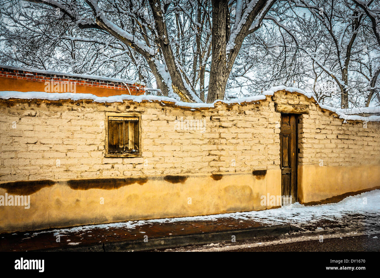 Eine Schnee-Szene verfügt über einen sehr alten und charmanten Adobe-Wand und Holztür führt in Hof im historischen Viertel, Santa Fe, NM Stockfoto