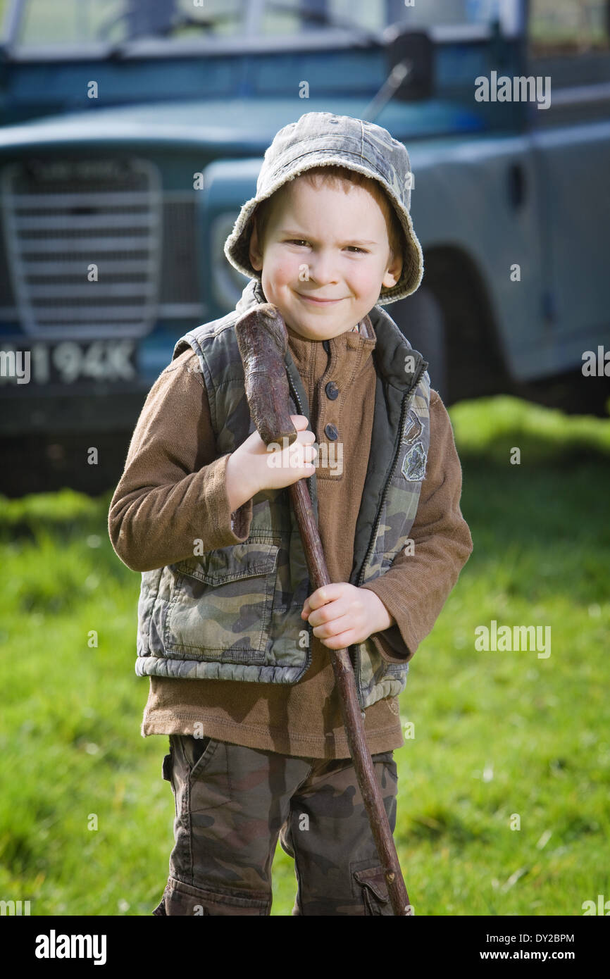 Ein 5 Jahre alter Junge in der typischen Landschaft Kleidung außerhalb hält einen Stock Stockfoto