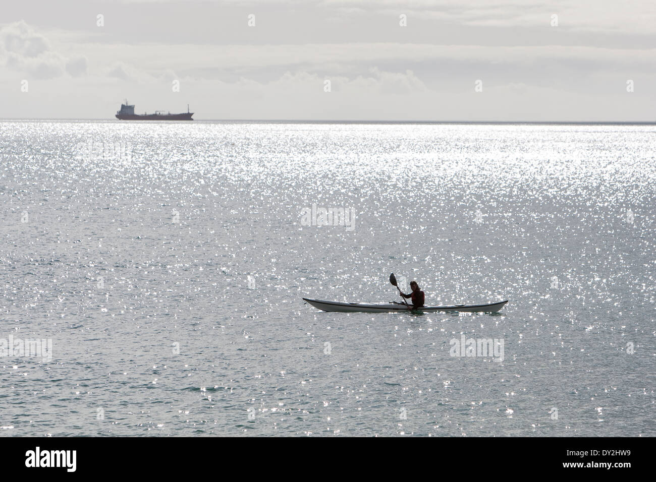 Ein Kajakfahrer sitzt in seinem Kajak Maenporth Strand, Falmouth, während ein Schiff am Horizont sitzt. Stockfoto