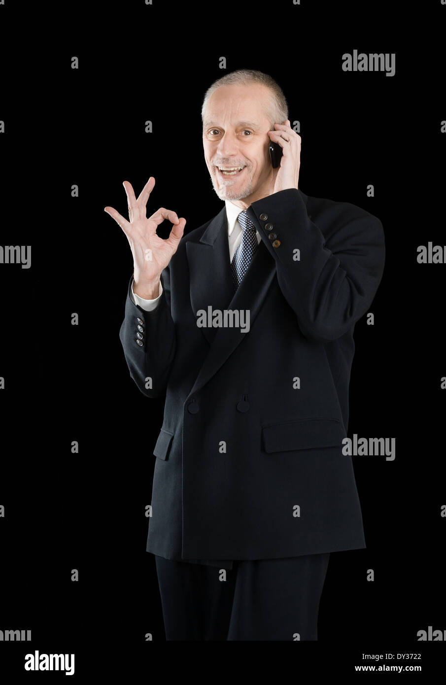 Eine liebenswürdige Geschäftsmann im schwarzen Anzug, lächelnd auf Handy und zeigt die OK Zeichen mit der Hand auf schwarzem Hintergrund Stockfoto