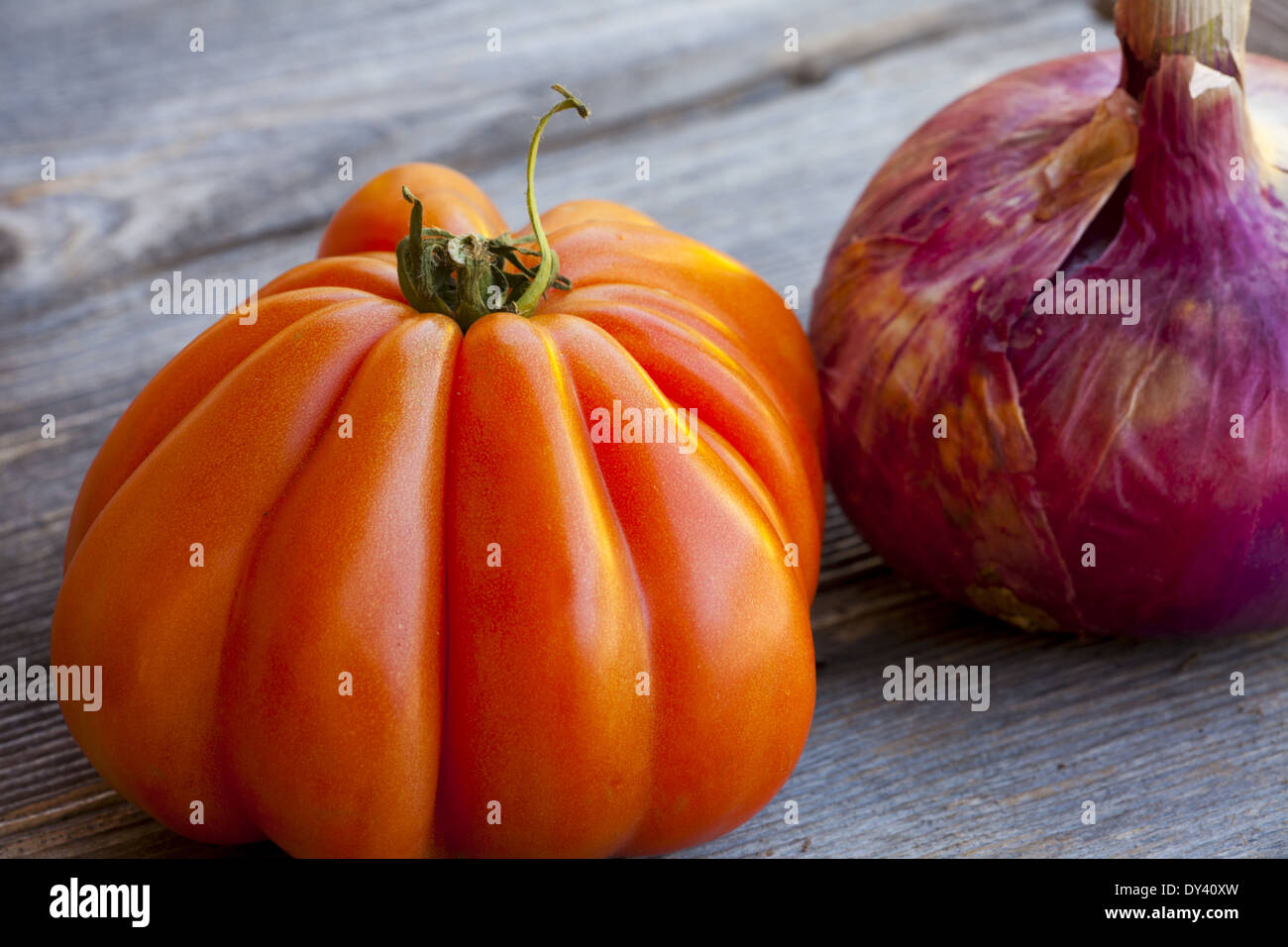 Ein Beefsteak Tomaten und eine ganze rote Zwiebel vom Wochenmarkt in Südfrankreich auf einem alten Holztisch Stockfoto