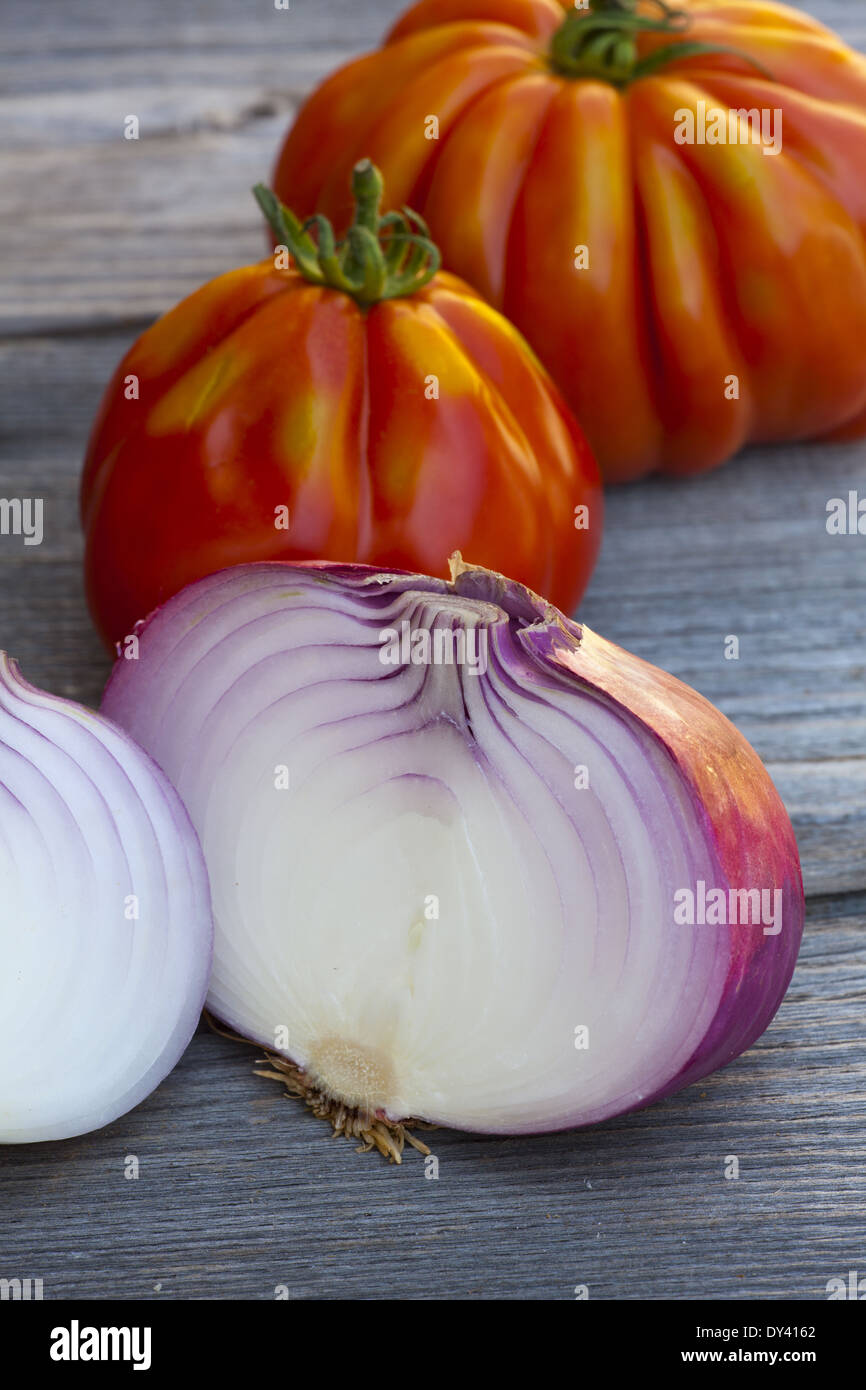 Coeur de Boeuf Tomaten und große rote Zwiebeln vom Wochenmarkt in Südfrankreich auf einem alten Holztisch Stockfoto