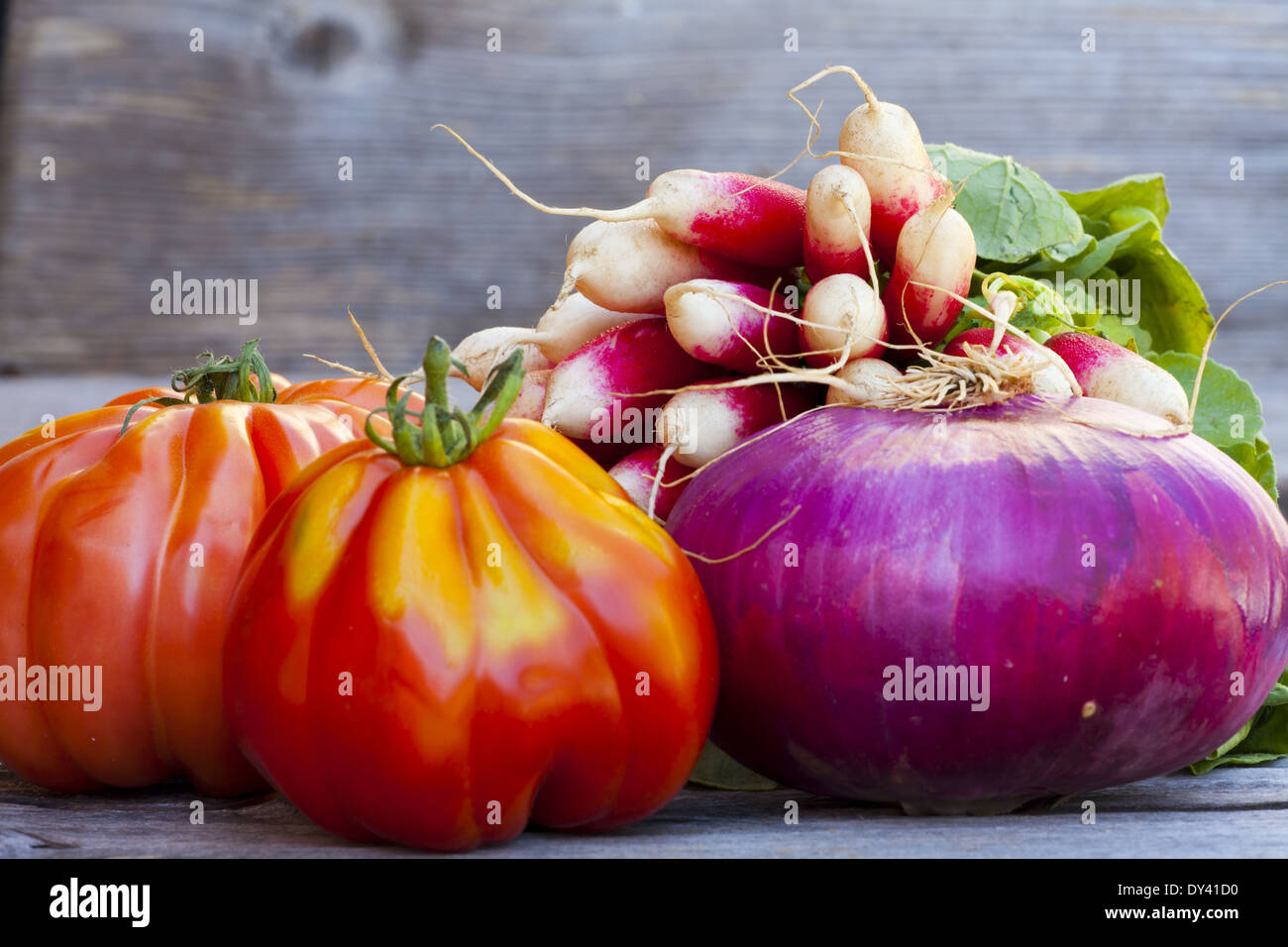 Coeur de Boeuf Tomaten, große rote Zwiebeln und Radieschen frisch vom Wochenmarkt auf einem alten Holztisch Stockfoto
