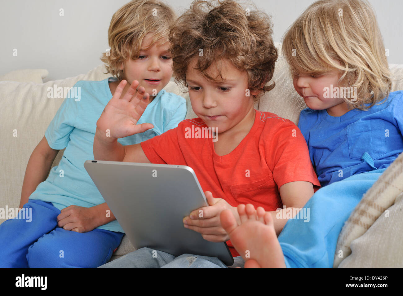 Ein ca. 8-9 Jahre alt spielt ein Spiel auf einem Touch-Screen-Tablette. Seine jüngeren Brüder beobachten jede Bewegung intensiv Stockfoto