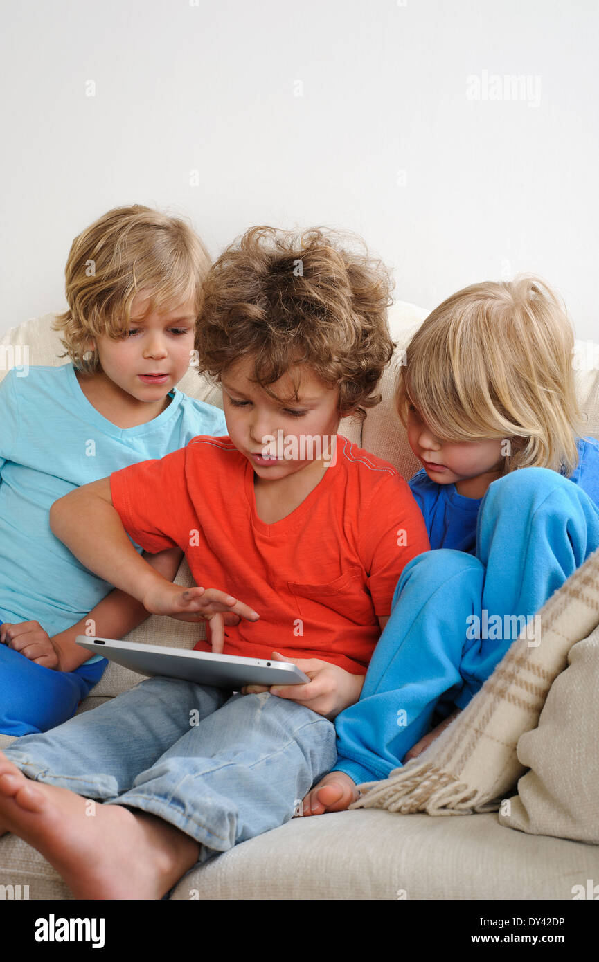 Ein ca. 8-9 Jahre alt spielt ein Spiel auf einem Touch-Screen-Tablette. Seine jüngeren Brüder beobachten jede Bewegung intensiv Stockfoto